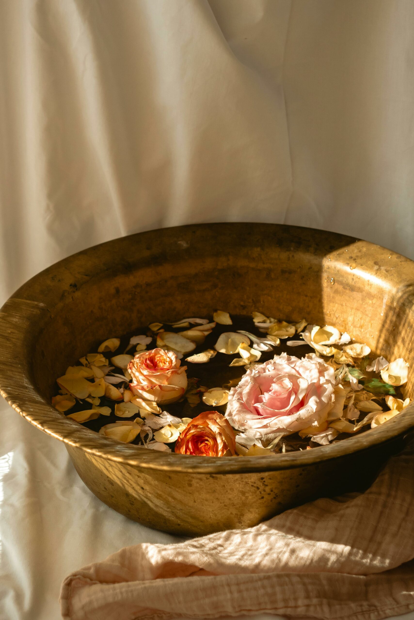 Elegant bronze basin with floating rose petals in warm lighting, ideal for spa and relaxation themes.